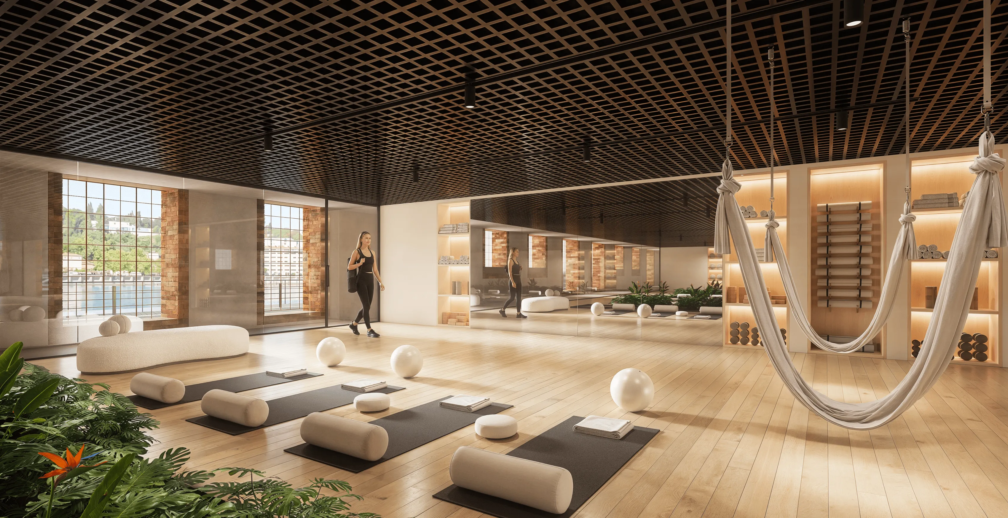 Modern wellness and yoga studio with wooden flooring, a black lattice ceiling, large mirrored walls, exercise mats, cushions, yoga balls, and aerial hammocks, creating a serene and elegant space for relaxation and mindful movement.